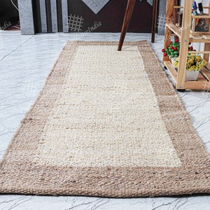 May include: A natural fiber rug with a light beige center and a brown border. The rug is made of woven jute and is perfect for adding a touch of natural texture to any room.