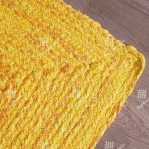 May include: A yellow and orange woven rug with a textured surface. The rug has a braided edge and is made of natural fibres.