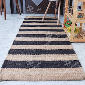 May include: A black and natural jute striped rug with a woven texture. The rug is laid out on a light gray tiled floor.