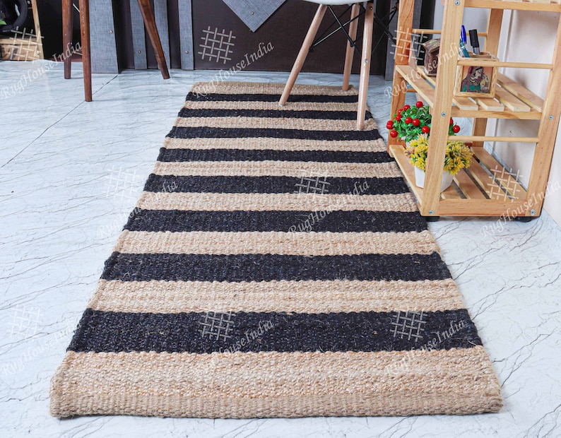 May include: A black and natural jute striped rug with a woven texture. The rug is laid out on a light gray tiled floor.