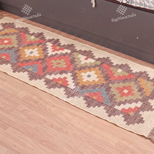 May include: A beige and brown patterned rug with colorful geometric designs. The rug has fringe on the ends and is made of natural fibers.