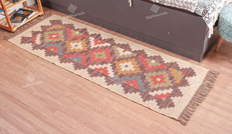 May include: A beige and brown patterned rug with colorful geometric designs. The rug has fringe on the ends and is made of natural fibers.