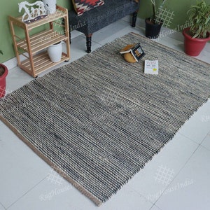 May include: A rectangular area rug featuring a textured, woven pattern in alternating stripes of dark charcoal gray and natural beige fibers. The rug has a thick, braided construction with a visible horizontal weave and a simple, clean-edged finish.