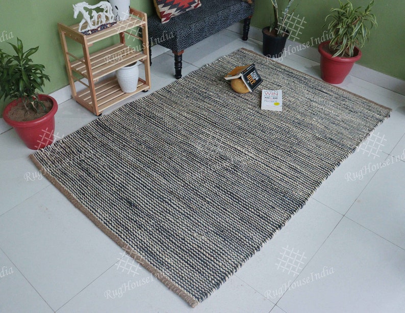 May include: A rectangular area rug featuring a textured, woven pattern in alternating stripes of dark charcoal gray and natural beige fibers. The rug has a thick, braided construction with a visible horizontal weave and a simple, clean-edged finish.