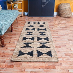 Puede incluir: Una alfombra de yute negra y beige con un patr&oacute;n geom&eacute;trico de tri&aacute;ngulos. La alfombra est&aacute; sobre un suelo de madera.