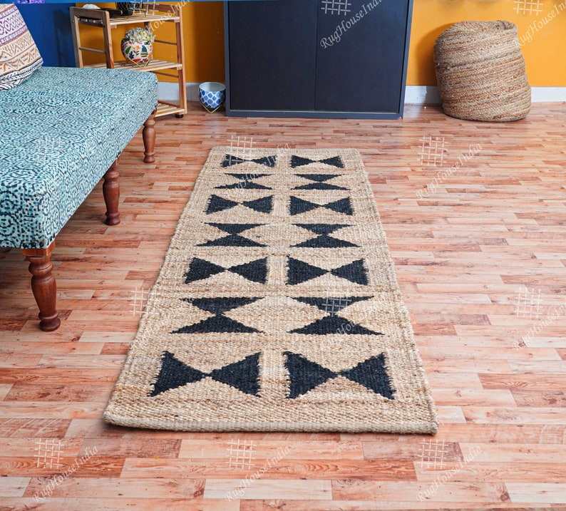 Puede incluir: Una alfombra de yute negra y beige con un patr&oacute;n geom&eacute;trico de tri&aacute;ngulos. La alfombra est&aacute; sobre un suelo de madera.