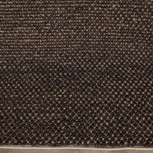 May include: Close-up of a textured, dark brown rug with a woven pattern. The rug has a neutral beige border and sits on a light brown tiled floor. The rug's surface is a mix of dark and light brown fibers.