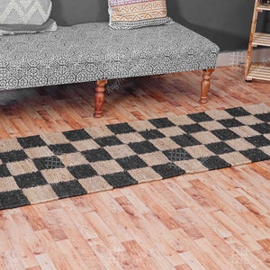 Puede incluir: Una alfombra a cuadros de color negro y yute natural con textura tejida. La alfombra est&aacute; colocada sobre un suelo de madera.