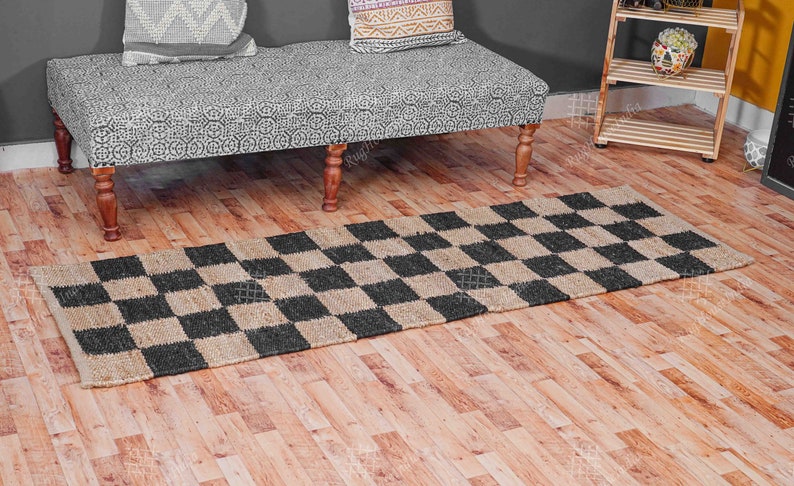 Puede incluir: Una alfombra a cuadros de color negro y yute natural con textura tejida. La alfombra est&aacute; colocada sobre un suelo de madera.