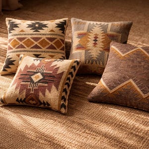 Puede incluir: Cuatro cojines decorativos cuadrados con patrones geométricos en tonos marrón, beige y óxido. Los cojines presentan diseños en zigzag, diamantes e inspirados en tribus, colocados sobre una alfombra tejida texturizada.