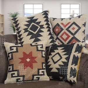 Op de afbeelding: Vier decoratieve kussens met geometrische patronen in zwart, wit en rood op een bruine bank. De kussens zijn gemaakt van een geweven stof met een textuur.