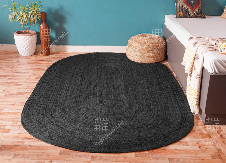May include: An oval-shaped area rug in a solid black color, featuring a braided texture throughout its surface. The rug is constructed with concentric loops that follow the oval outline, creating a uniform and consistent pattern across the entire piece.