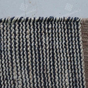 May include: A rectangular woven rug featuring a repeating vertical striped pattern in alternating dark navy blue and off-white fibers. The rug has a thick, textured braided weave construction with a solid tan border along the right edge.