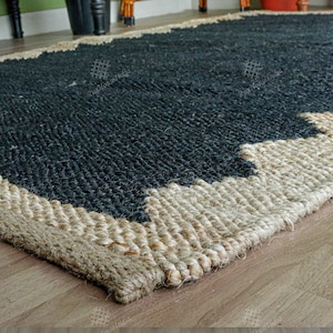 May include: A black and natural jute rug with a geometric pattern. The rug has a thick, woven texture and a natural, earthy look.