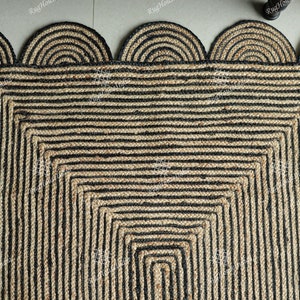 May include: A square jute rug with a black and natural color striped pattern. The rug has a scalloped edge with a black and natural color striped design.