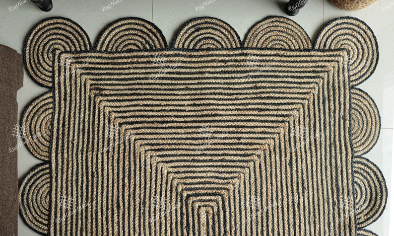 May include: A square jute rug with a black and natural color striped pattern. The rug has a scalloped edge with a black and natural color striped design.