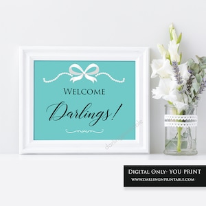 May include: A printable welcome sign with a turquoise background, white bow, and pearl accents. The text reads "Welcome Darlings!" in black cursive font.