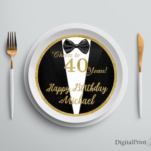 May include: A white round plate with a black and gold circular design. The design features a tuxedo with a bow tie and the text "Cheers to 40 Years! Happy Birthday Michael".