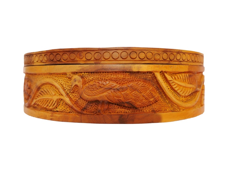 May include: A round wooden box with intricate carvings of peacocks and leaves. The box is made of light brown wood and has a lid.