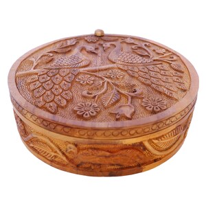 May include: A round wooden box with a carved design of peacocks and flowers. The box has a hinged lid and is made of light brown wood.