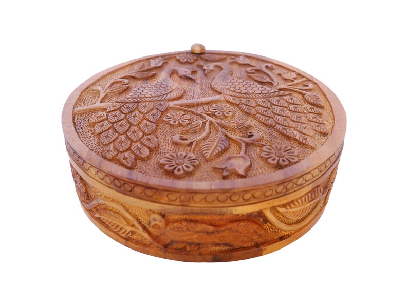 May include: A round wooden box with a carved design of peacocks and flowers. The box has a hinged lid and is made of light brown wood.