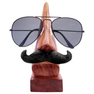 May include: Wooden stand shaped like a face with sunglasses and a mustache, designed to hold eyeglasses.