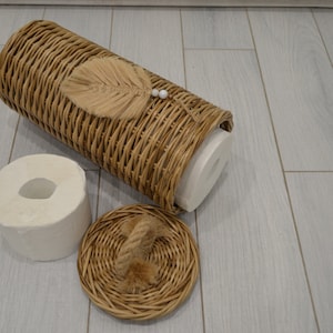 Puede incluir: Una cesta de mimbre con tapa y un rollo de papel higi&eacute;nico dentro. La cesta tiene una hoja decorativa y detalles de perlas.