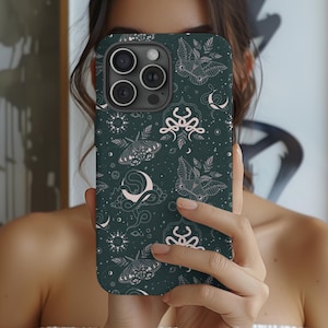 May include: Dark green phone case featuring a repeating pattern of moths, moons, and celestial designs in light pink and white. The case has a matte finish and a camera cutout.