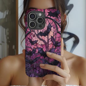 May include: A phone case featuring a stained-glass design with bats in shades of purple, pink, and black. The case has a glossy finish and a dark border. The design includes a tree-like structure with bats in flight, creating a spooky, gothic aesthetic.