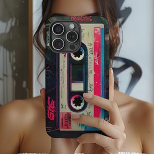 May include: A phone case featuring a retro cassette tape design. The case has a black border and a colorful cassette tape graphic with red, pink, and blue accents. The text "GTS" and other Japanese text are visible on the case.