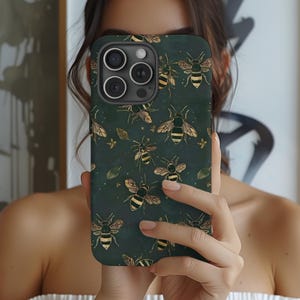 May include: A dark green phone case with a repeating pattern of gold and black bees and leaves. The case has a matte finish and a camera cutout. The design is a nature-inspired pattern.