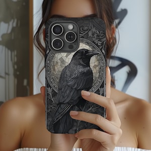 May include: Black phone case featuring a detailed illustration of a raven. The raven is set against a stained-glass style background with floral accents. The case has a matte finish and a dark color palette.