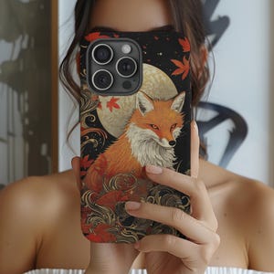 Pode incluir: Uma capa de telefone preta com uma ilustração colorida de uma raposa em frente a uma lua cheia. A raposa é cercada por padrões florais e ondulados estilizados. A capa do telefone tem um recorte para a lente da câmera.