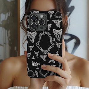 May include: A black phone case featuring a white shark tooth pattern. The case has a camera lens cutout and a white outline around the edges.