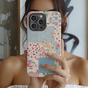以下が含まれることがあります： ピンク、ブルー、ホワイトの花柄のパッチワークデザインのスマホケース。ケースにはカメラの切り抜きと白い背景があります。