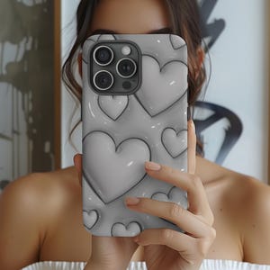 Könnte beinhalten: Eine graue iPhone-Hülle mit einem 3D-Herz-Muster. Die Hülle hat einen Ausschnitt für das Kameraobjektiv und einen erhöhten Rand an den Kanten.