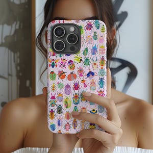 Pode incluir: Uma capa de smartphone com fundo rosa claro coberta por um padrão repetitivo de besouros e insetos coloridos em vários tons de azul, verde, amarelo, laranja e roxo, com um recorte preto para a lente da câmera na parte superior.