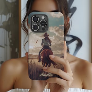 May include: A personalized phone case with a photo of a woman riding a horse in a field. The case has a brown background with a blue sky and white clouds. The woman is wearing a cowboy hat and a blue shirt. The text "Amelia" is printed on the bottom of the case.