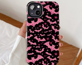 May include: A black phone case with a repeating pattern of pink bats and stars. The bats are in different sizes and positions, with their wings outstretched. The stars are also pink, enhancing the design. The case has cutouts for the camera and buttons.