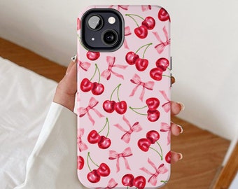 May include: Pink phone case with a pattern of cherries and bows. The case has a cutout for the camera lens.
