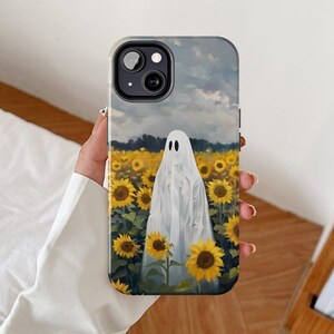 May include: A white ghost figure stands in a field of yellow sunflowers. The ghost is wearing a white sheet and has a faint smile. The background is a cloudy sky.