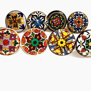 May include: A collection of eight decorative ceramic cabinet knobs. Each knob features a unique, colorful, and intricate floral or geometric pattern in shades of blue, yellow, red, green, and orange. The knobs are round with a metal base.