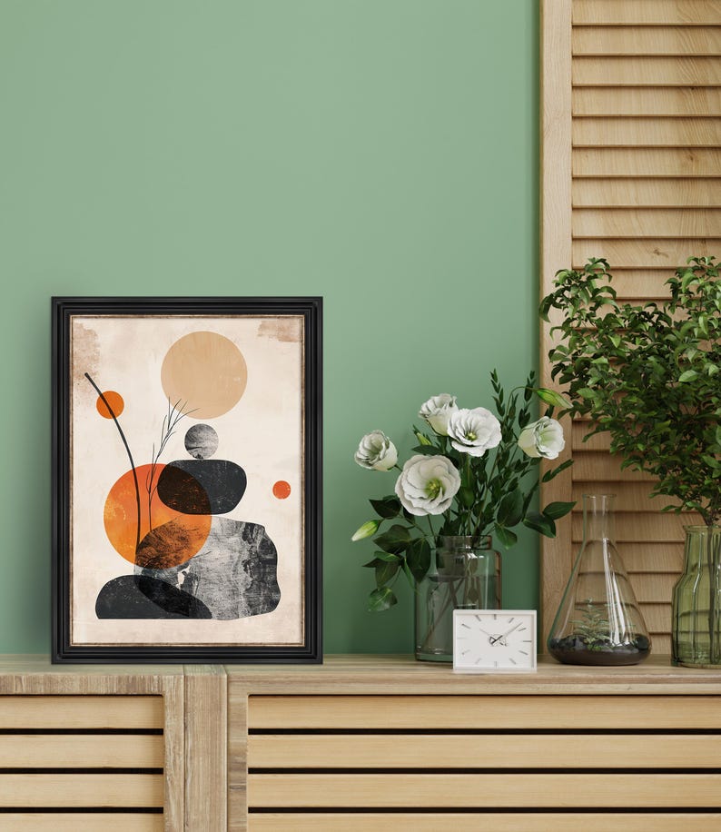 May include: A framed abstract print with a beige background and black, orange, and brown geometric shapes. The print is in a black frame and is hanging on a green wall.