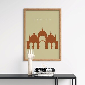 May include: A framed print with a beige background and a brown silhouette of a building with multiple domes. The text "VENICE" is printed in brown at the top of the print.