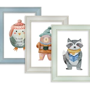 May include: Three framed watercolour prints of winter animals. The prints show an owl, a bear with a mug, and a raccoon reading a book. The frames are light blue, off-white, and light green.