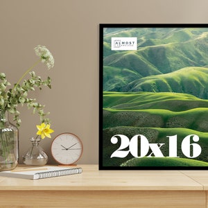 May include: A framed print featuring a landscape of rolling green hills under a bright sky. The print is 20 x 16 inches and has a black frame. The text "ALMOST FRAMELESS" is at the top. The number "20x16" is at the bottom.