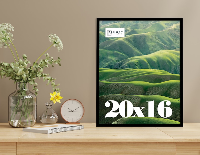 May include: A framed print featuring a landscape of rolling green hills under a bright sky. The print is 20 x 16 inches and has a black frame. The text "ALMOST FRAMELESS" is at the top. The number "20x16" is at the bottom.