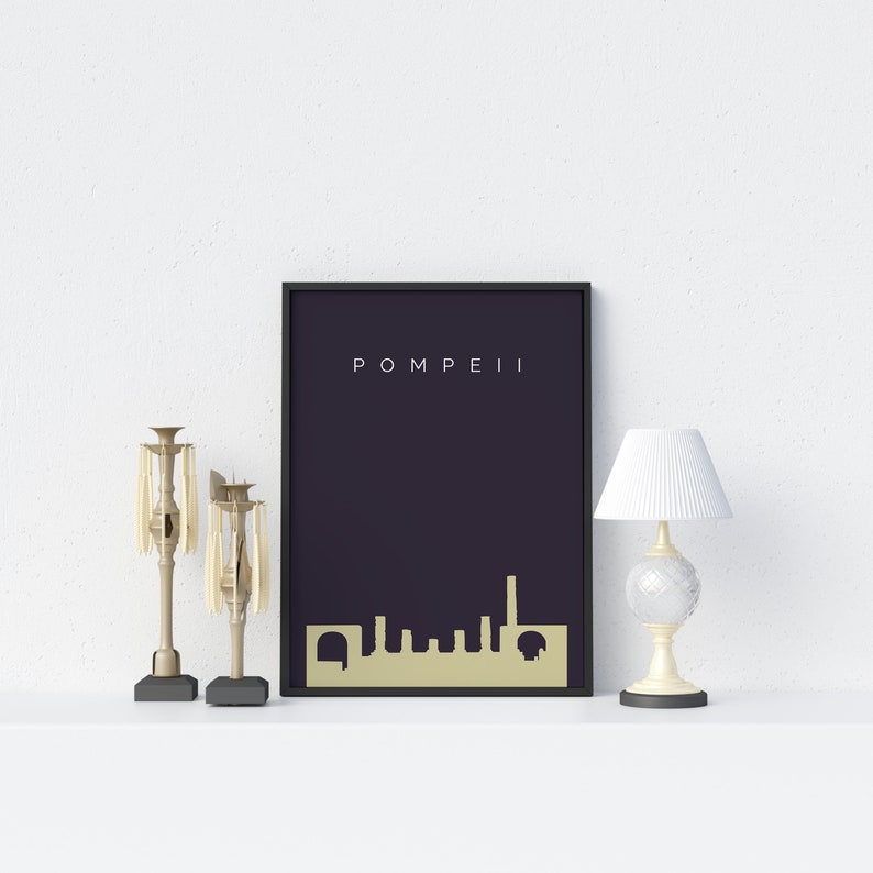 May include: A framed art print with the word "POMPEII" in white text. The print features a gold-colored skyline silhouette against a dark purple background. Decorative candle holders and a small lamp are on the shelf.