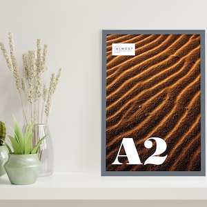 May include: A gray framed poster with a close-up photo of sand dunes. The poster is labeled "A2" and "Almost Frameless".