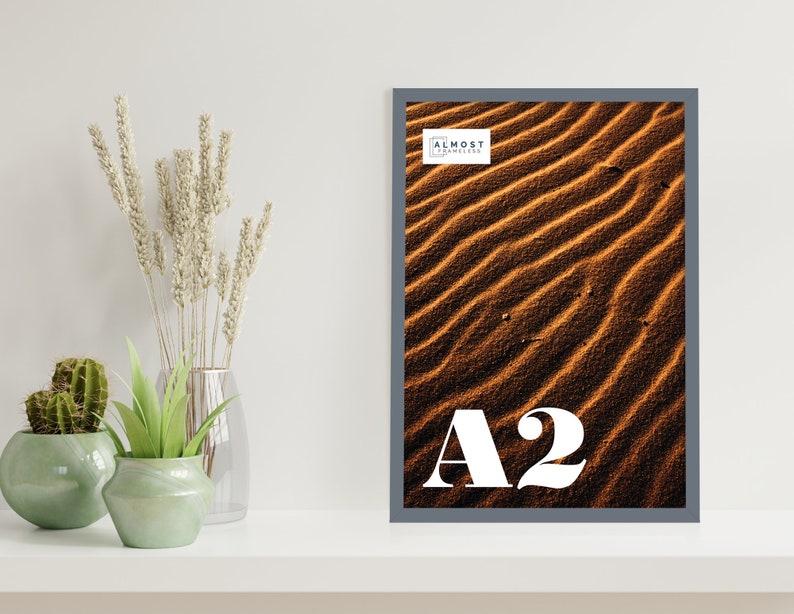 May include: A gray framed poster with a close-up photo of sand dunes. The poster is labeled "A2" and "Almost Frameless".